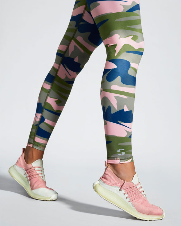 Camufarre activewear print. Model wearing women's sustainable leggings featuring a unique camo activewear print created with a purpose by Scultura. Inspired by the ocean and designed to raise awareness of the environmental impact of single use plastic. Created with premium technical Italian fabric made with 100% regenerated yarn from recycled plastic bottles (rPET). Side iew.