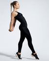 Model standing sideways wearing The Balletto, a sustainable full length black gym top and the Debutto, black gym leggings. Made with recycled premium sports wear fabric, created with yarn from recovered ocean fishing nets.