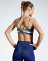 Model wearing Camufarre Sustainable Sports Bra with cross back straps. Featuring a one off camo activewear print created with a purpose by Scultura. Inspired by the ocean and designed to raise awareness of the environmental impact of single use plastic. Created with premium technical Italian fabric made with 100% regenerated yarn from recycled plastic bottles (rPET). Back View.