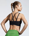 Black sustainable sports bra featuring cross back straps. Model wearing sustainable gym bra. Made in the UK with Premium Italian sportswear fabric created with ECONYL regenerated yarn. 