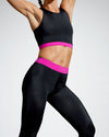 Model wearing pink and black sustainable gym crop. Rosa Nera is a longer length crop featuring a racer back and a fuchsia under bust band. Women’s Sustainable Activewear made to last with premium Italian sports tech fabric created with ECONYL Regenerated Yarn.  Front view.